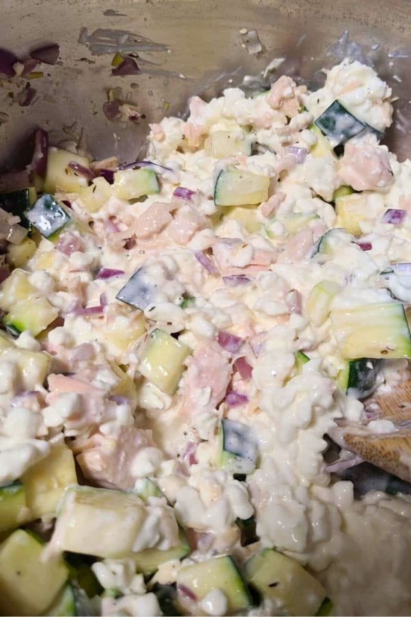 A close-up of a mixture containing diced zucchini, red onion, chicken pieces, and cottage cheese in a metal bowl—perfect as a fresh filling for your next Penne Tuna Pasta Bake.