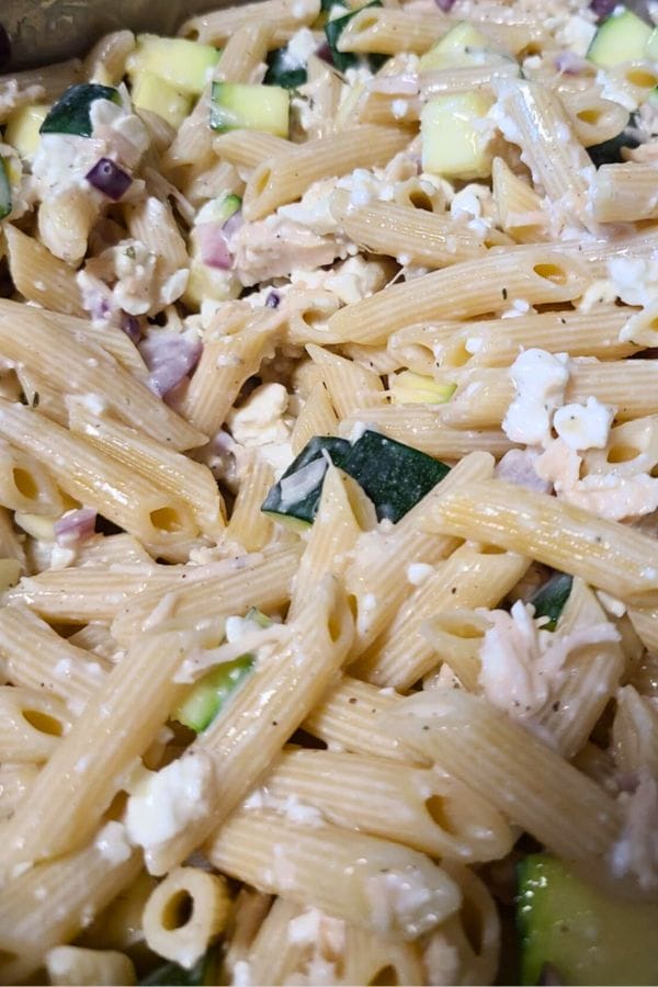 Close-up of Penne Tuna Pasta Bake featuring penne pasta mixed with diced zucchini, red onion, chicken, and crumbled white cheese.