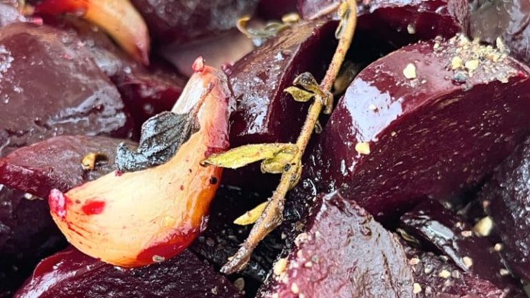 Close-up of Roasted Beets chunks with garlic cloves, fresh thyme, and cracked black pepper.