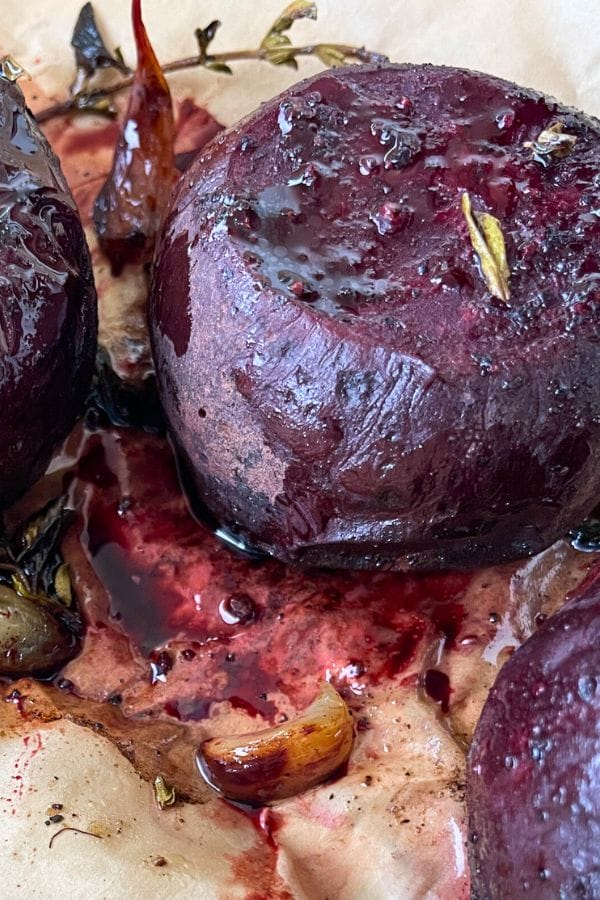 Close-up of roasted beets with herbs and garlic on parchment paper, highlighting their vibrant juices and slightly charred edges for a perfect Roasted Beets dish.