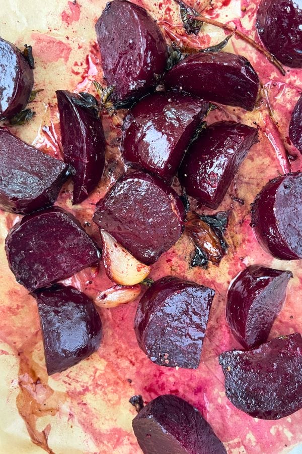 Roasted Beets: Roasted beetroot wedges and garlic cloves on parchment paper, glistening with oil and juice.