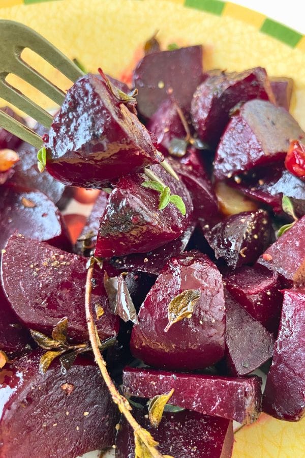 Close-up of roasted beetroot pieces, with a fork lifting one above the plate. Fresh herbs garnish the vibrant roasted beets, highlighting their rich color and flavor.