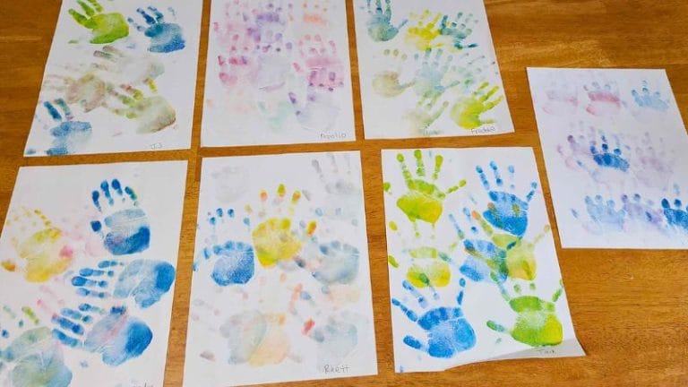 Eight sheets of paper with colorful handprints in various sizes and arrangements are displayed on a wooden table, perfect for inspiring creativity in lesson plans on Andy Warhol.
