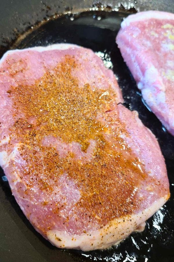 Taco Pork Chops with seasoning are sizzling in a black skillet, filling the kitchen with mouthwatering aromas.