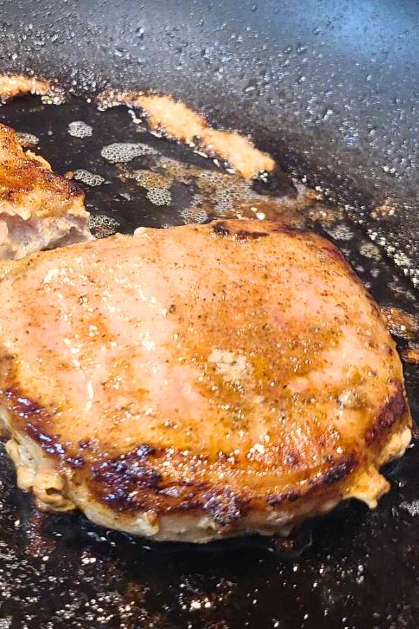 A seasoned Taco Pork Chop browning in a hot skillet, with oil and flavorful juices bubbling around it.