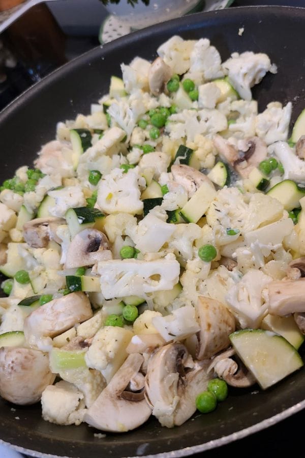 A pan filled with chopped cauliflower, zucchini, mushrooms, and green peas being cooked together—a fresh veggie blend perfect for a Tuna Casserole Without Noodles.