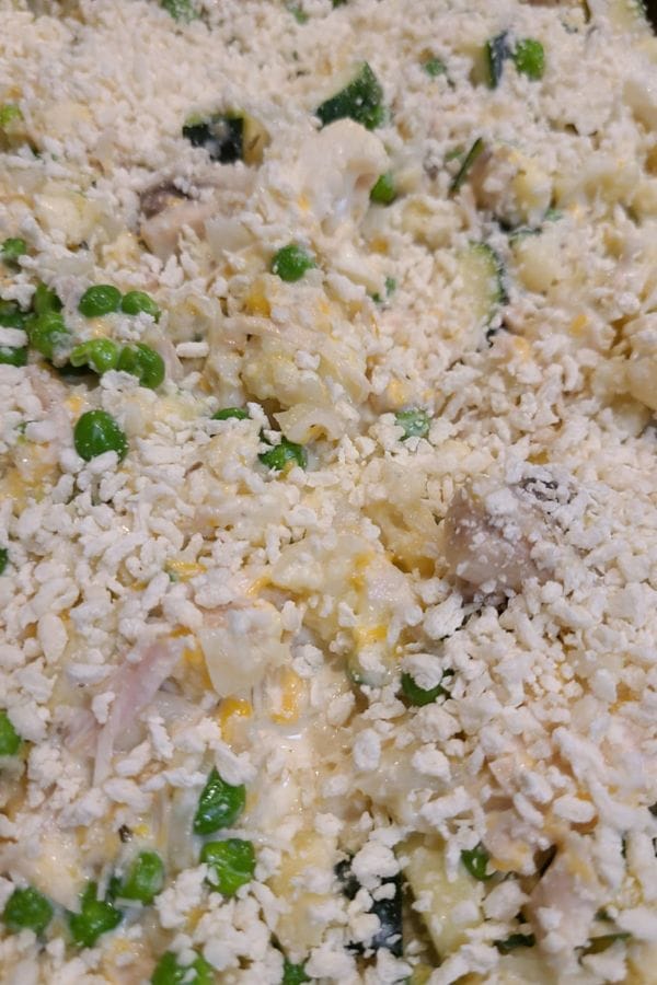 Close-up of a Tuna Casserole Without Noodles, topped with shredded cheese and breadcrumbs, showing peas, green beans, and pieces of cauliflower.