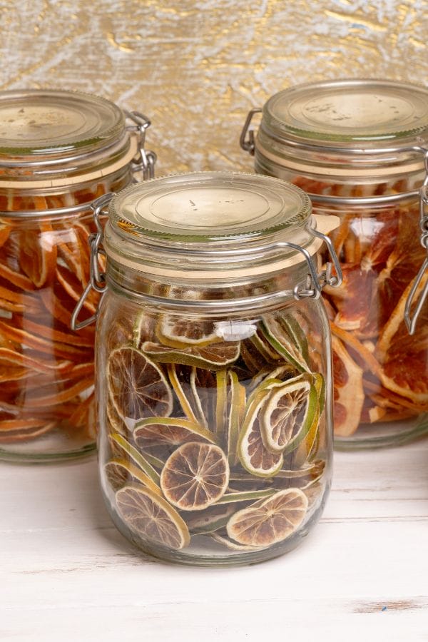 Three glass jars with metal clasps display dried citrus slices—lime in the front and orange in the back—showcasing a stylish way to store dehydrated food for easy access and freshness.
