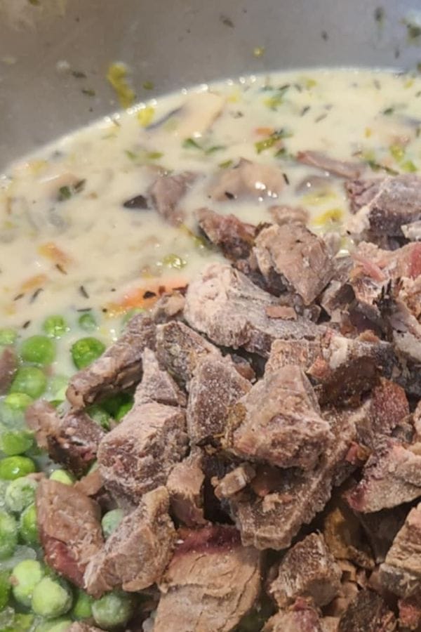 Chopped cooked meat, green peas, and a creamy sauce with herbs and vegetables in a metal bowl—perfect for crafting a hearty Leftover Brisket Pot Pie.