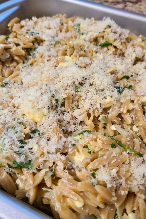 A close-up of Tuna and Orzo Pasta mixed with greens and topped with grated cheese in a metal tray.