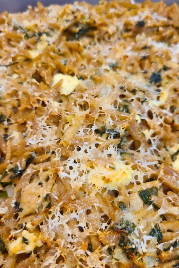 Close-up of a Tuna and Orzo Pasta bake topped with melted cheese, visible herbs, and browned edges.