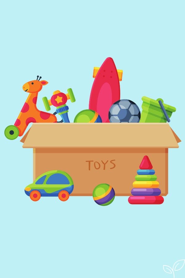 A cardboard box labeled "Toys" filled with various toys, including a giraffe ride-on, skateboard, ball, toy car, stacking rings, a bucket, and a copy of "The Little Engine That Could.