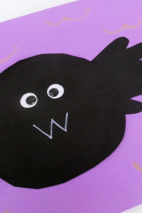 A craft fish made from black paper with googly eyes and a white "W" mouth, set on a purple background—perfect inspiration for a Handprint Bat or other fun Halloween crafts.
