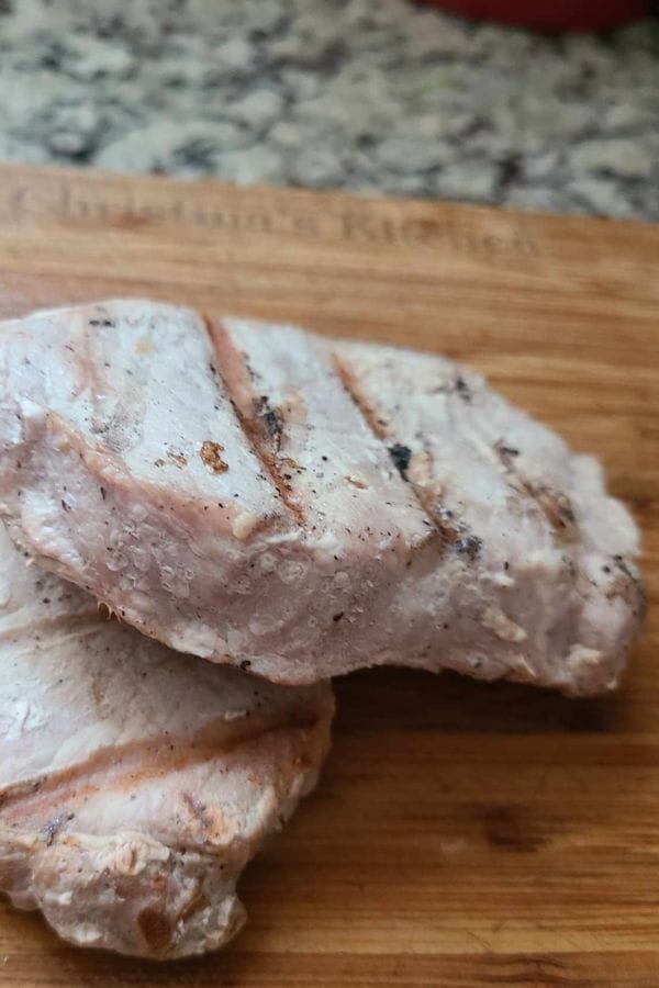 Two pieces of grilled, lightly seasoned chicken breast on a wooden cutting board—perfect for adding to your favorite dishes or pairing with a comforting Leftover Pork Chop Soup.