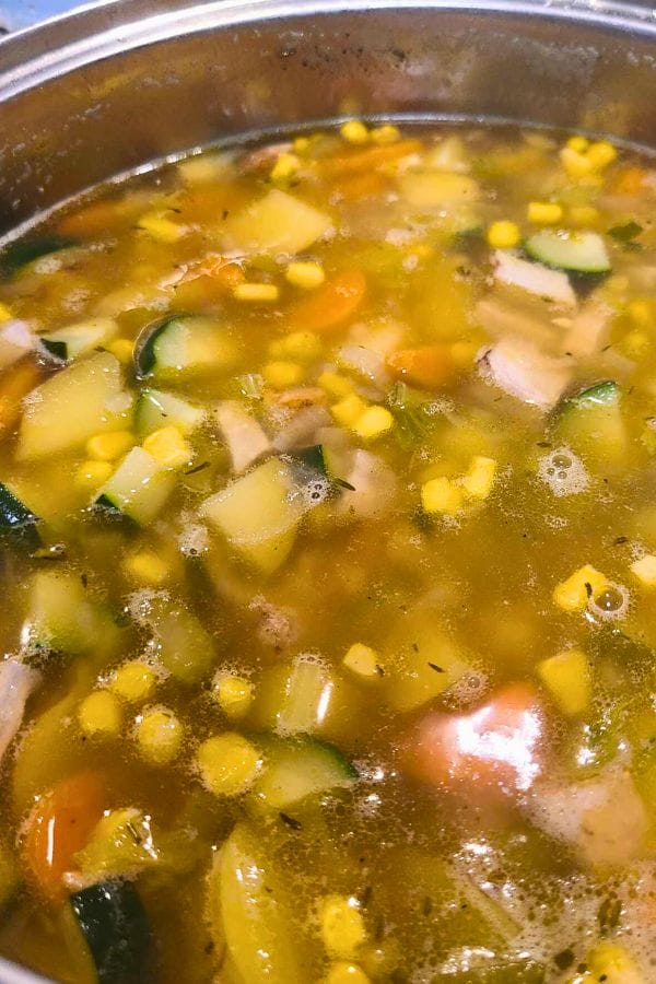 A close-up of a pot of Leftover Pork Chop Soup with visible zucchini, corn, carrots, and savory broth.