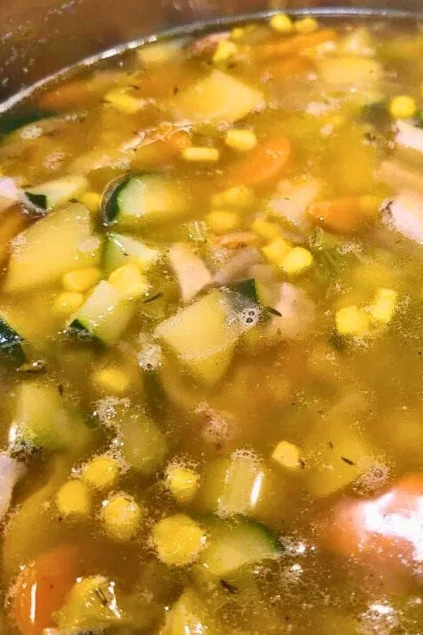 A close-up of vegetable soup with visible chunks of zucchini, corn, carrots, and potatoes in a clear broth—perfect for adding diced meat from leftover pork chop recipes for extra flavor and heartiness.