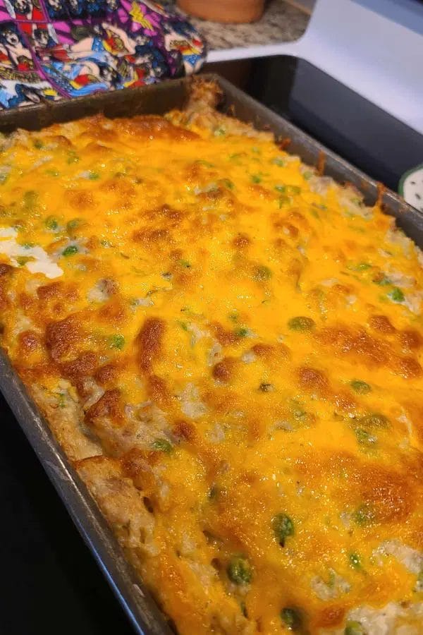 A casserole dish filled with a baked mixture topped with melted cheddar cheese, showing visible peas and a golden-brown crust—one of the best Freezer Friendly Tuna Recipes for easy, delicious meals anytime.