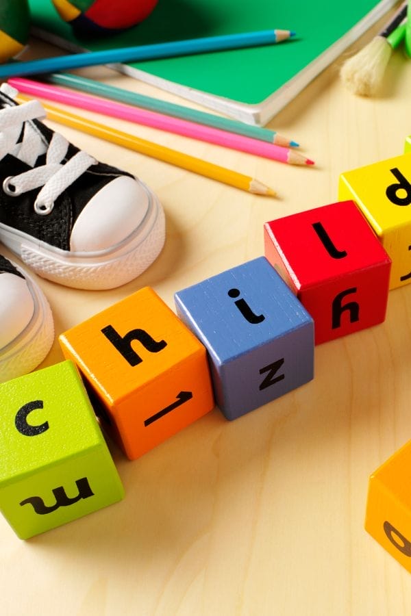 Colorful alphabet blocks spelling "child," paired with a sneaker, colored pencils, and a green notebook on a light wooden surface—perfect for vibrant childcare advertising.