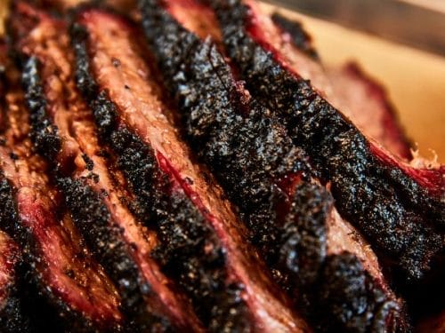 Close-up of several slices of smoked beef brisket with a dark, seasoned crust and visible marbling, arranged on brown parchment paper—perfect for creating delicious Leftover Brisket Appetizers.