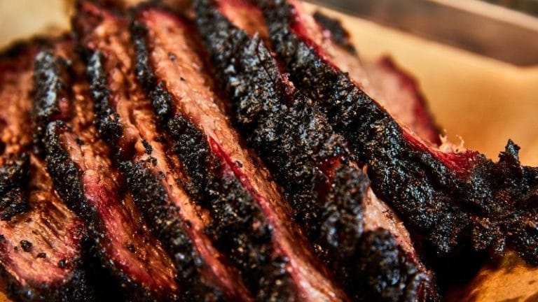 Close-up of several slices of smoked beef brisket with a dark, seasoned crust and visible marbling, arranged on brown parchment paper—perfect for creating delicious Leftover Brisket Appetizers.