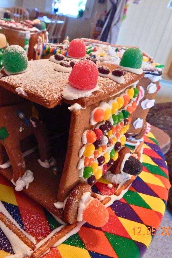 A gingerbread house decorated with colorful candies and gumdrops sits on a multicolored surface; powdered sugar is sprinkled on top—the perfect inspiration for lesson plans on gingerbread.