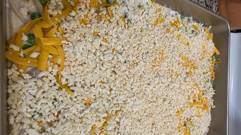 A casserole dish filled with Tuna Tetrazzini mixture, topped with crushed crackers and shredded cheddar cheese, ready to be baked.