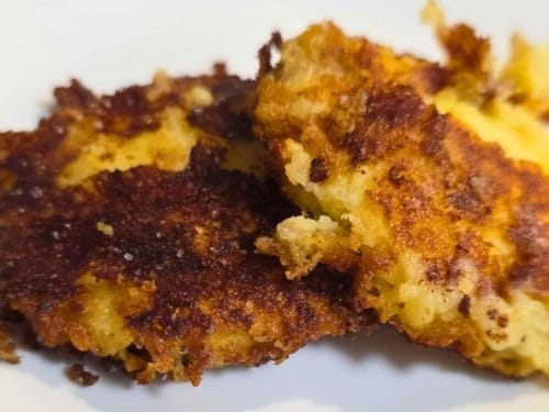 Two golden-brown Mashed Potato Cakes with crispy edges rest on a white plate.
