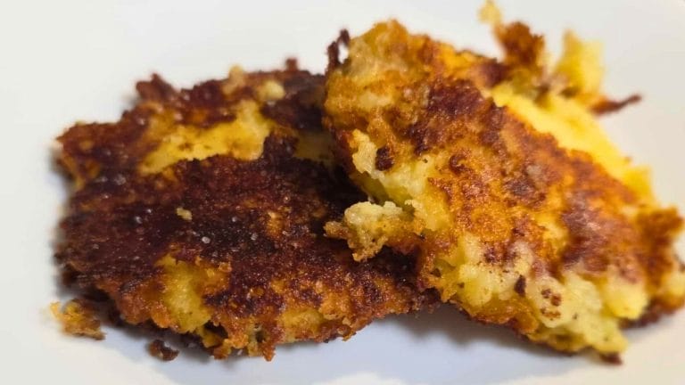 Two golden-brown Mashed Potato Cakes with crispy edges rest on a white plate.