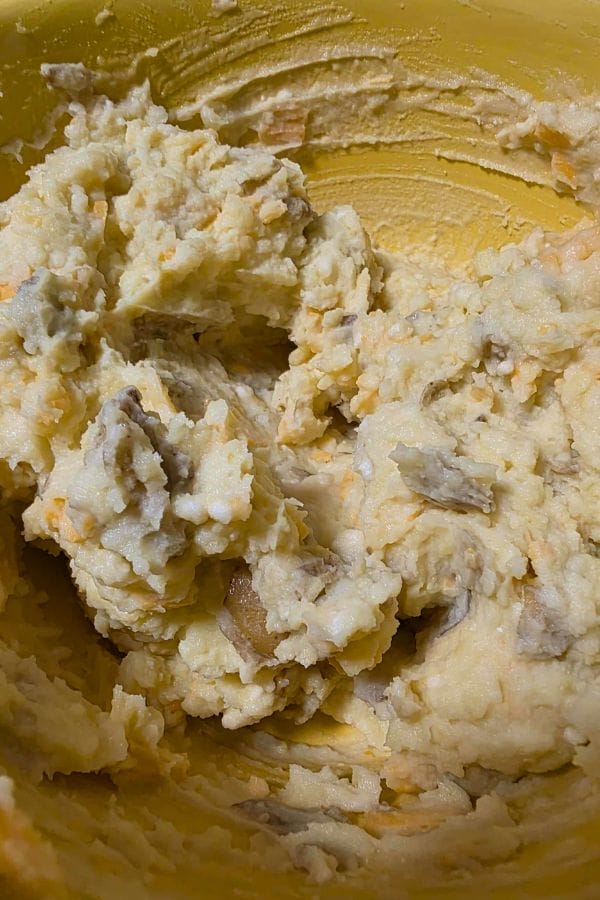 A close-up of chunky mashed potatoes and onions in a yellow mixing bowl, perfect for making flavorful Mashed Potato Cakes.