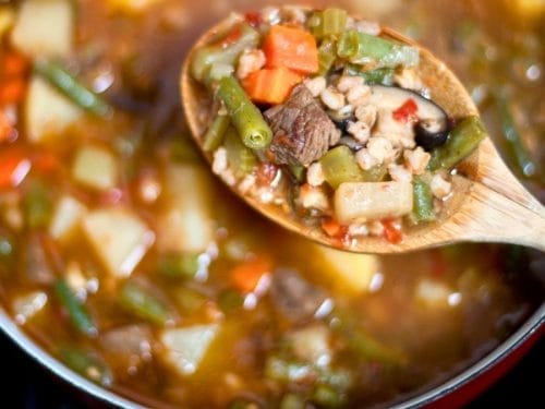 A wooden spoon holds a mix of vegetables and beef above a pot of chunky, colorful soup—one of the best winter comfort foods for kids.