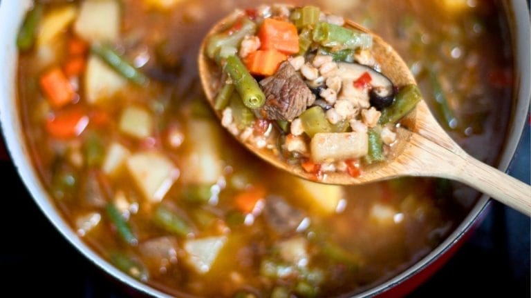 A wooden spoon holds a mix of vegetables and beef above a pot of chunky, colorful soup—one of the best winter comfort foods for kids.