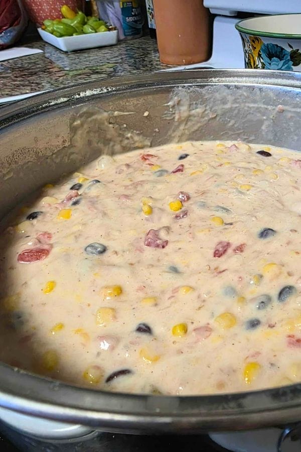 A pot filled with a creamy mixture of corn, black beans, diced tomatoes, and other ingredients—perfect for creating a flavorful Southwest Tuna Noodle Casserole—sits on a kitchen countertop.