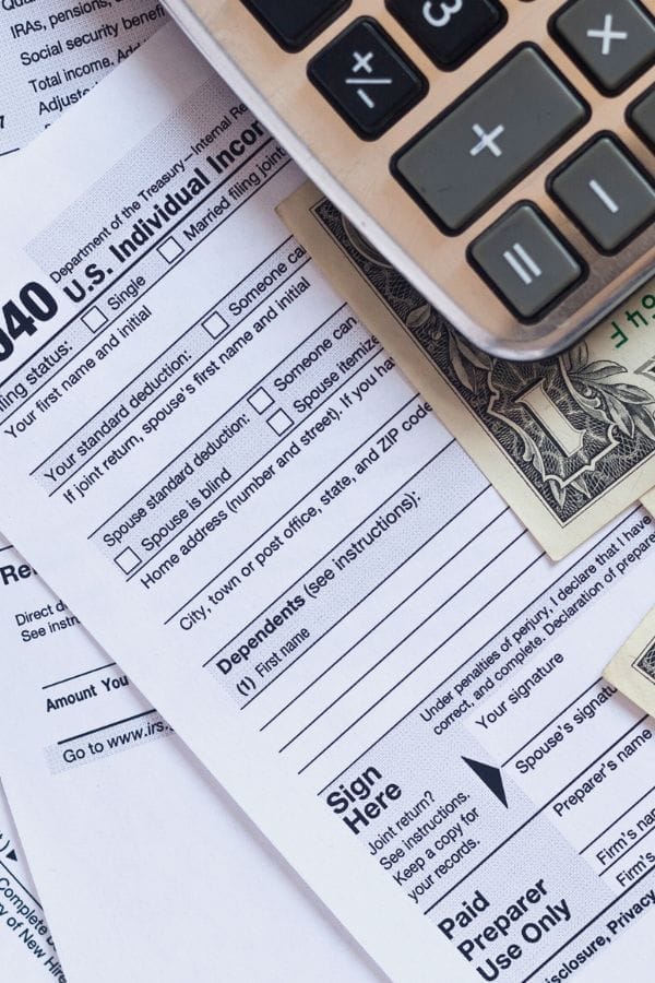 A close-up of a 1040 U.S. tax form, a calculator, and a twenty-dollar bill on a desk—perfect for organizing finances and finding Tax Tips for Home Daycare providers.
