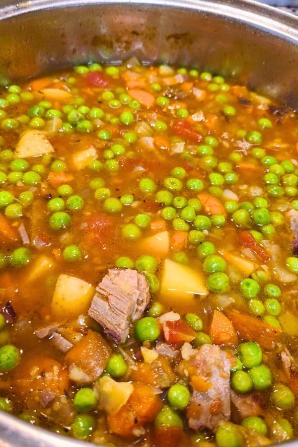 A close-up of a pot filled with hearty stew—green peas, chunks of meat, potatoes, carrots, and a tomato-based broth—perfect for those craving comforting Winter Soups.