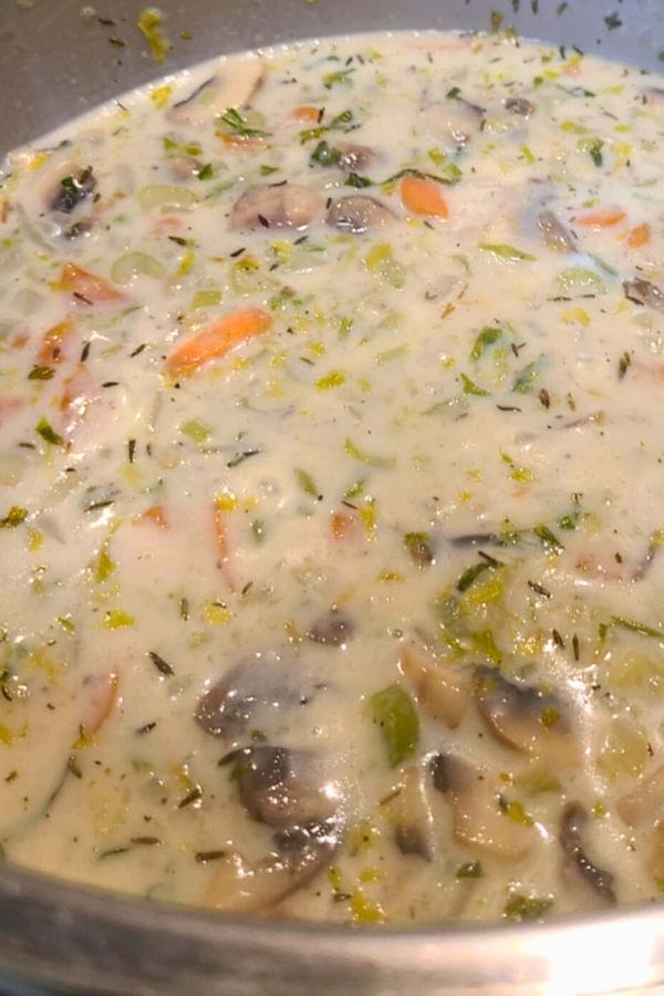 Close-up of a creamy Winter Soup with sliced mushrooms, carrots, celery, and herbs visible in the mixture.