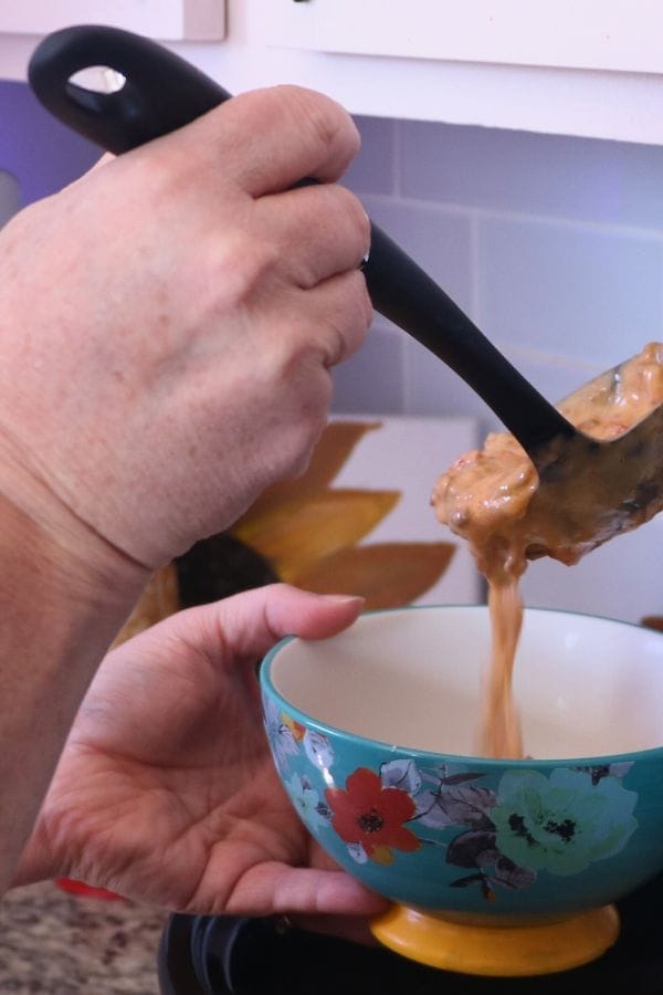 A person ladles thick, chunky soup into a ceramic bowl with a floral design.