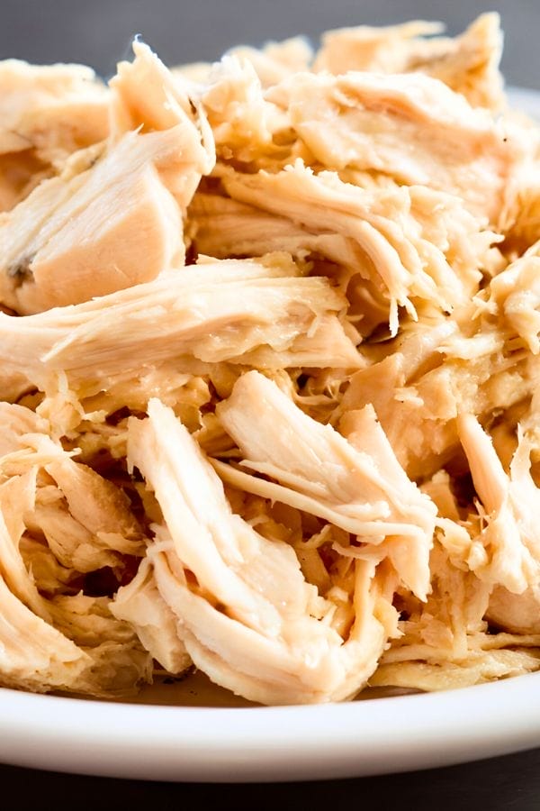 A close-up of shredded leftover chicken breast piled on a white plate.