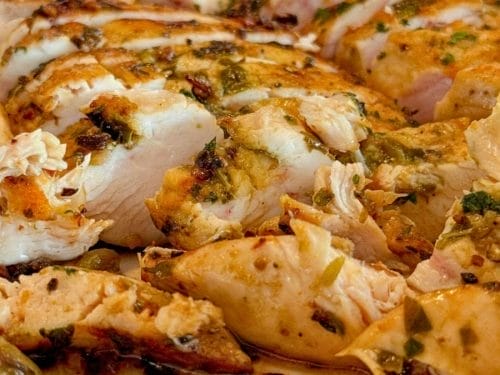 Close-up of sliced, seasoned cooked chicken breast with herbs and spices—perfect for inspiring creative leftover chicken ideas.