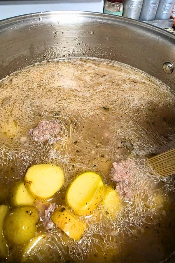 A pot of Loaded Zuppa Toscana Soup with sliced potatoes and ground meat simmering in a seasoned broth.